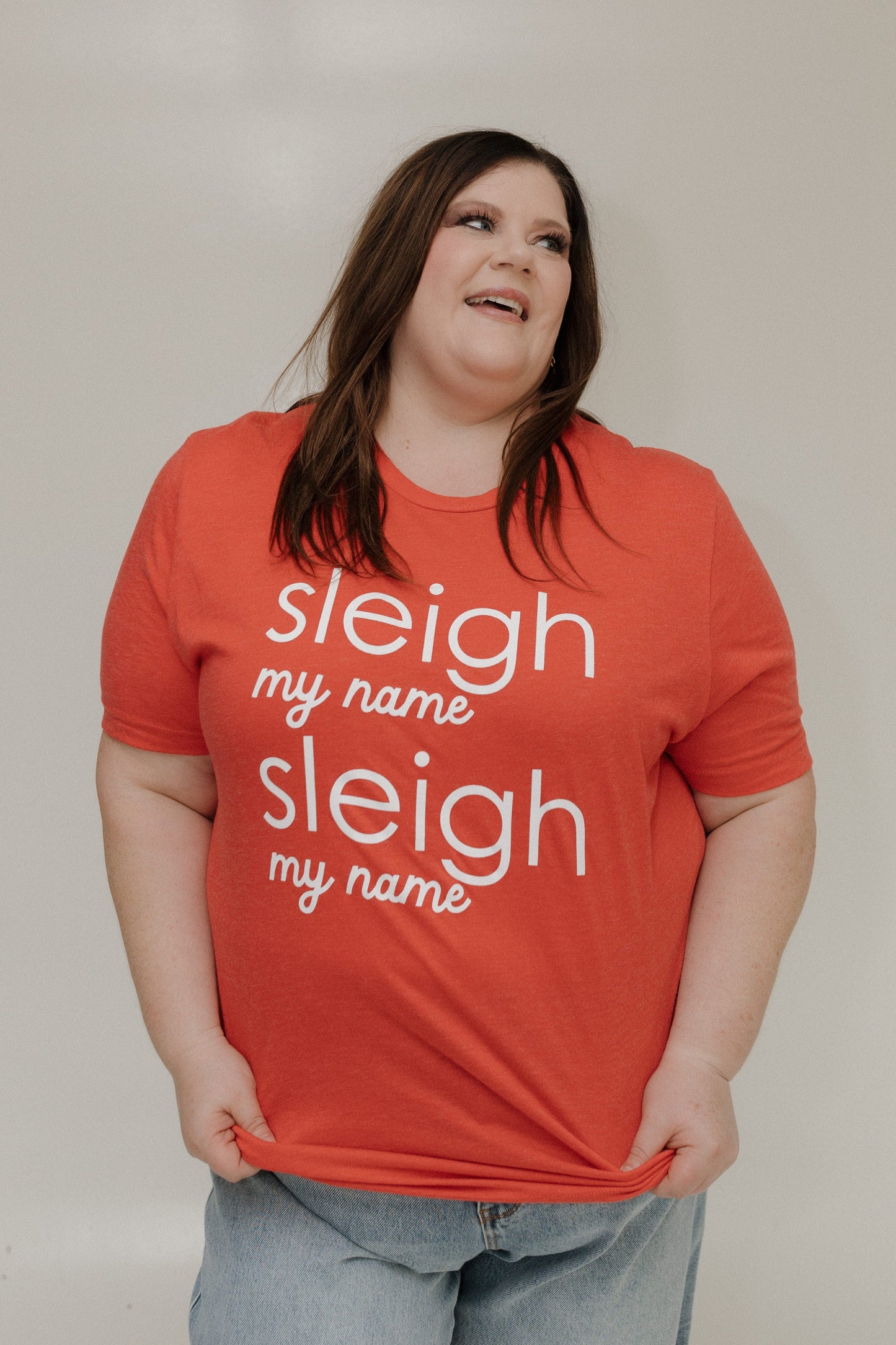 Person wearing a red t-shirt with 'sleigh my name' text on a plain background