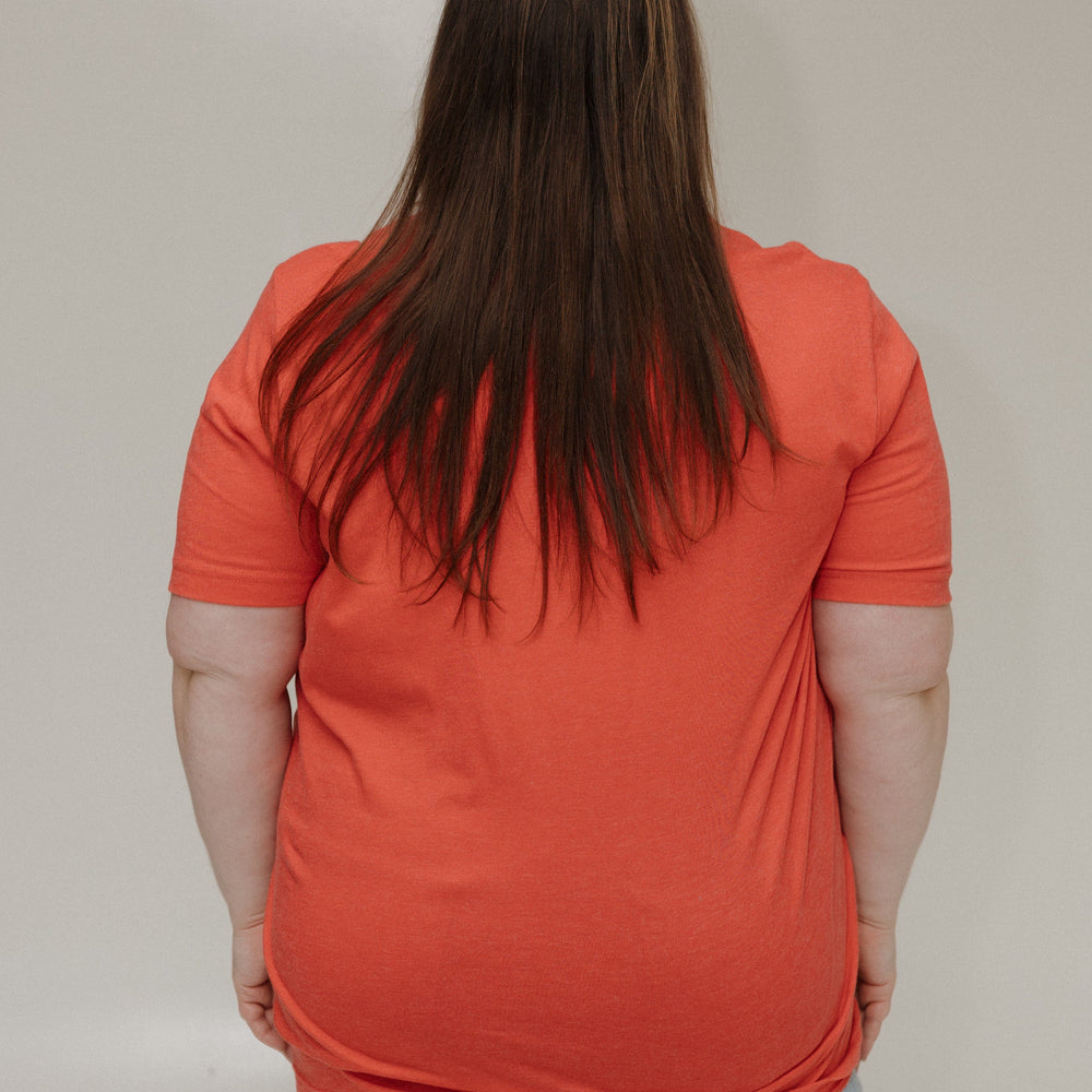 Person wearing an orange shirt and light blue jeans against a plain background
