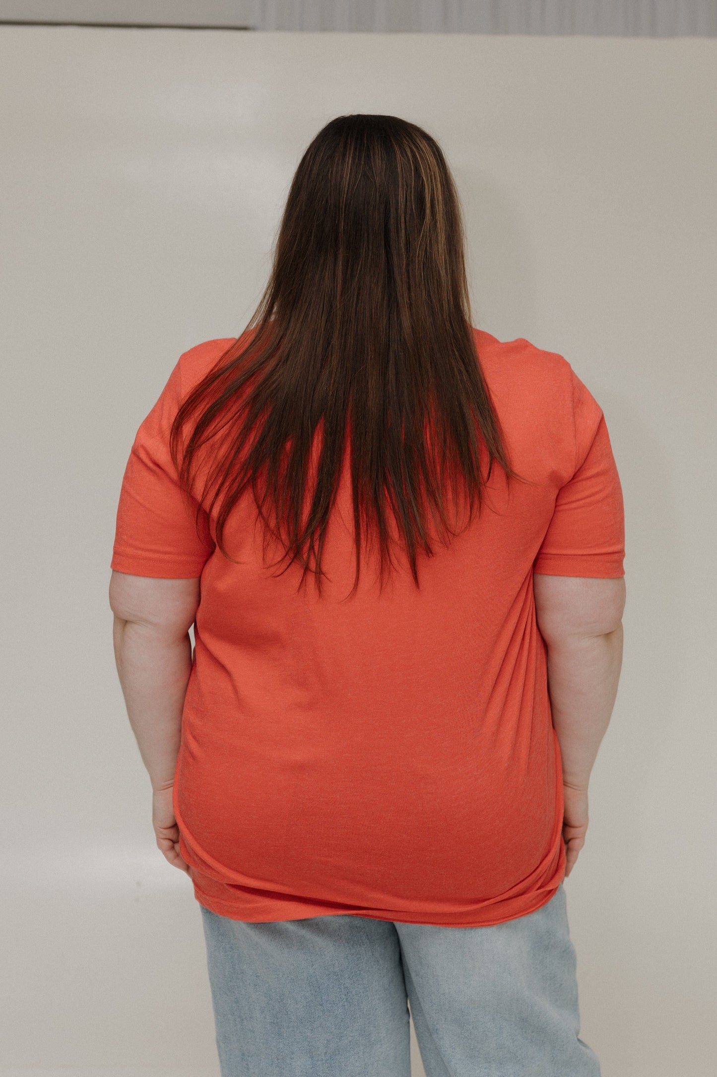 Person wearing an orange shirt and light blue jeans against a plain background