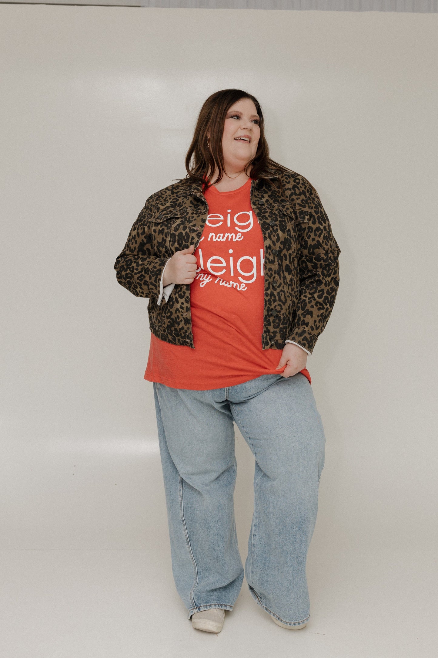 Person wearing a red shirt with text, leopard print jacket, and blue jeans on a white background