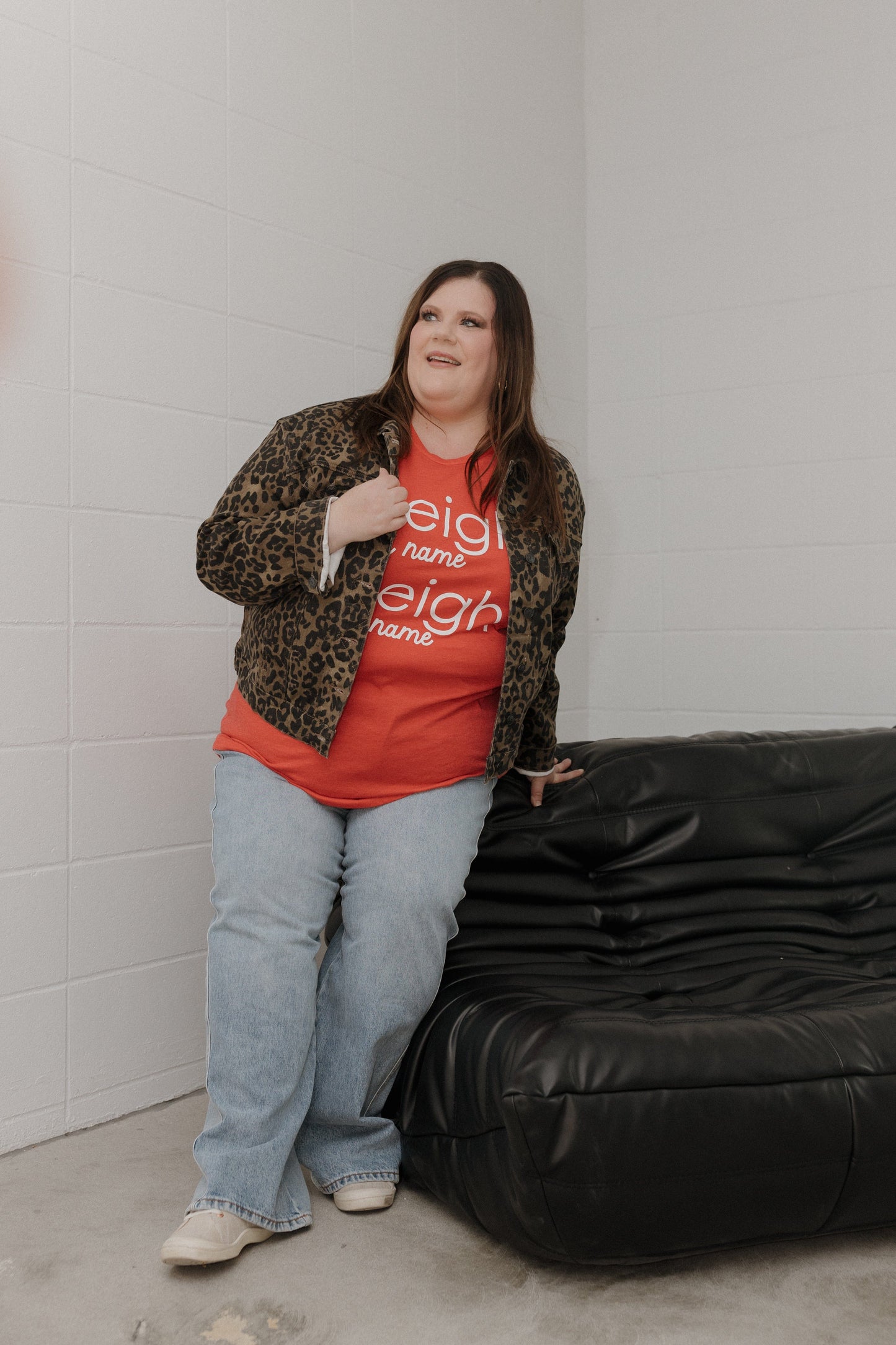 Woman wearing a red shirt with text and leopard print jacket leaning against a black bean bag chair.