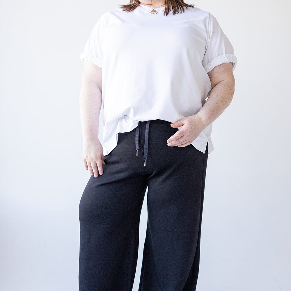 A person wearing a white shirt and black pants, made of lightweight spacer fabric for added comfort, stands smiling against a white background.