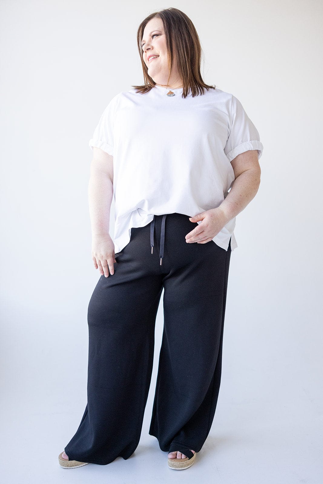 A person wearing a white shirt and black pants, made of lightweight spacer fabric for added comfort, stands smiling against a white background.