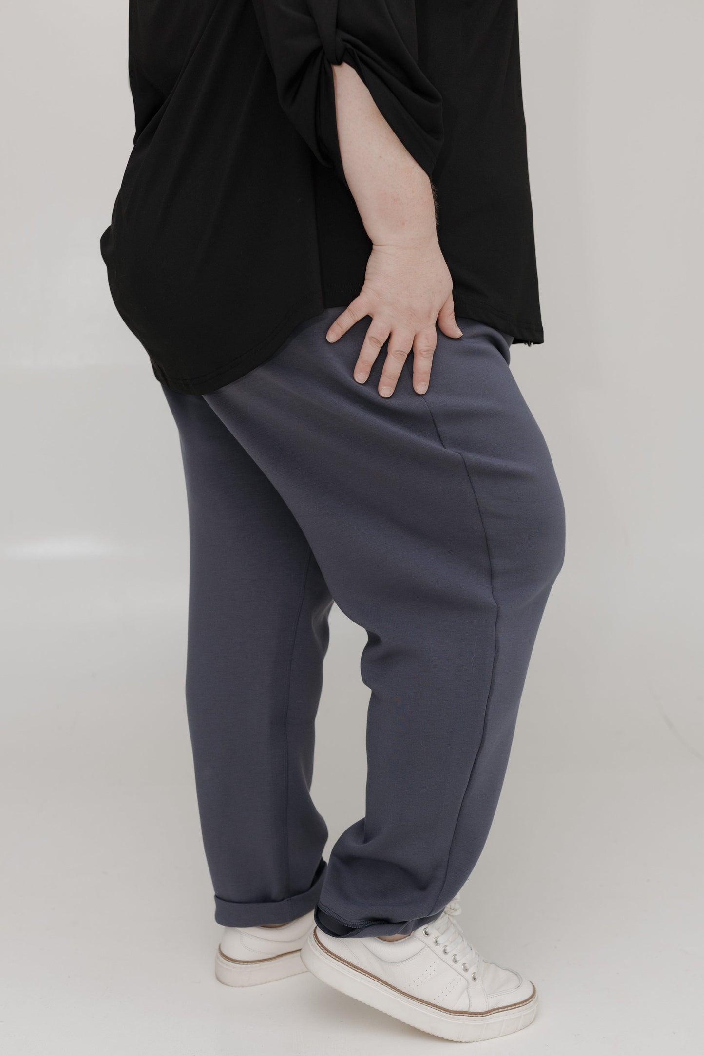 Person wearing a black top and gray pants on a white background