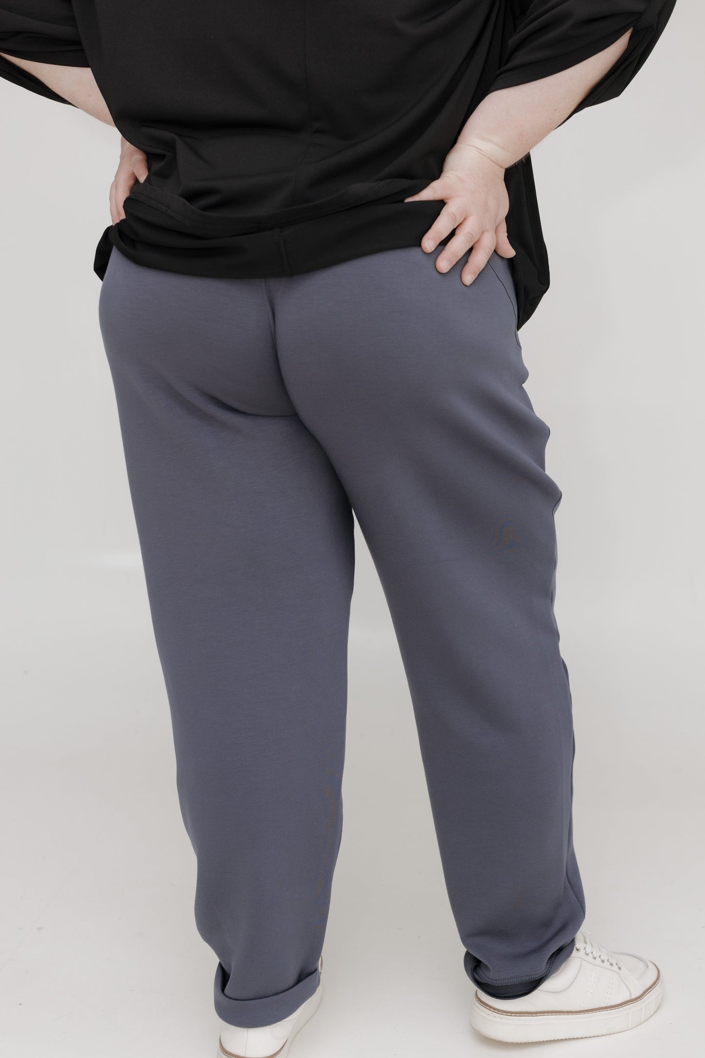 Person wearing a black top and gray pants on a white background