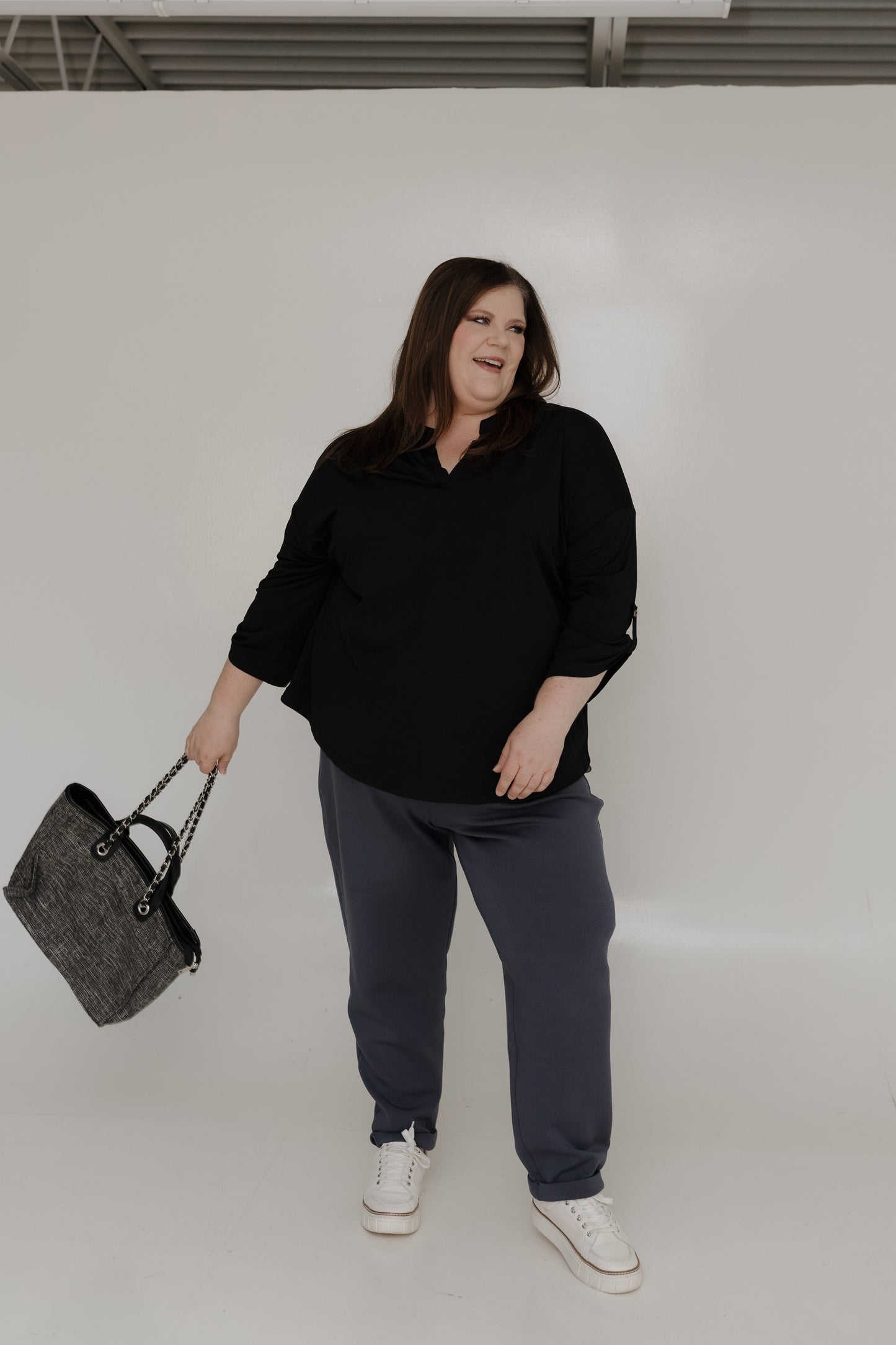 Person wearing a black shirt and gray pants, holding a gray bag against a white background