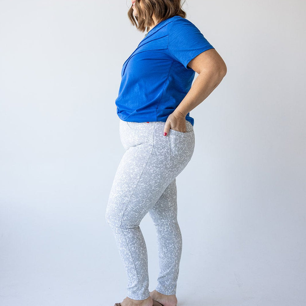 A person wearing a blue shirt and Spanx© Ankle Jean-ish® Legging in Speckled Grey, featuring tummy control, stands sideways against a white background.