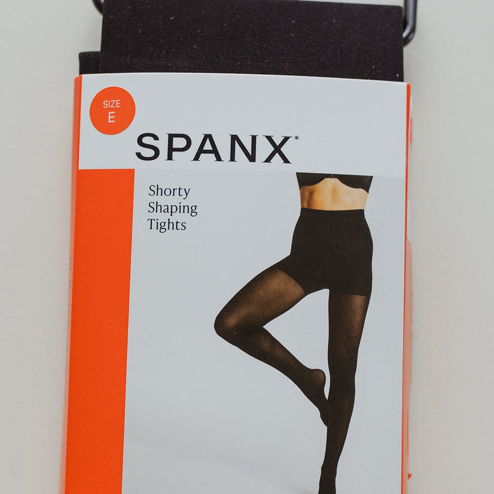 Package of Spanx size E shorty shaping tights with a comfort waistband and black hanger, offering medium support for a secure fit.