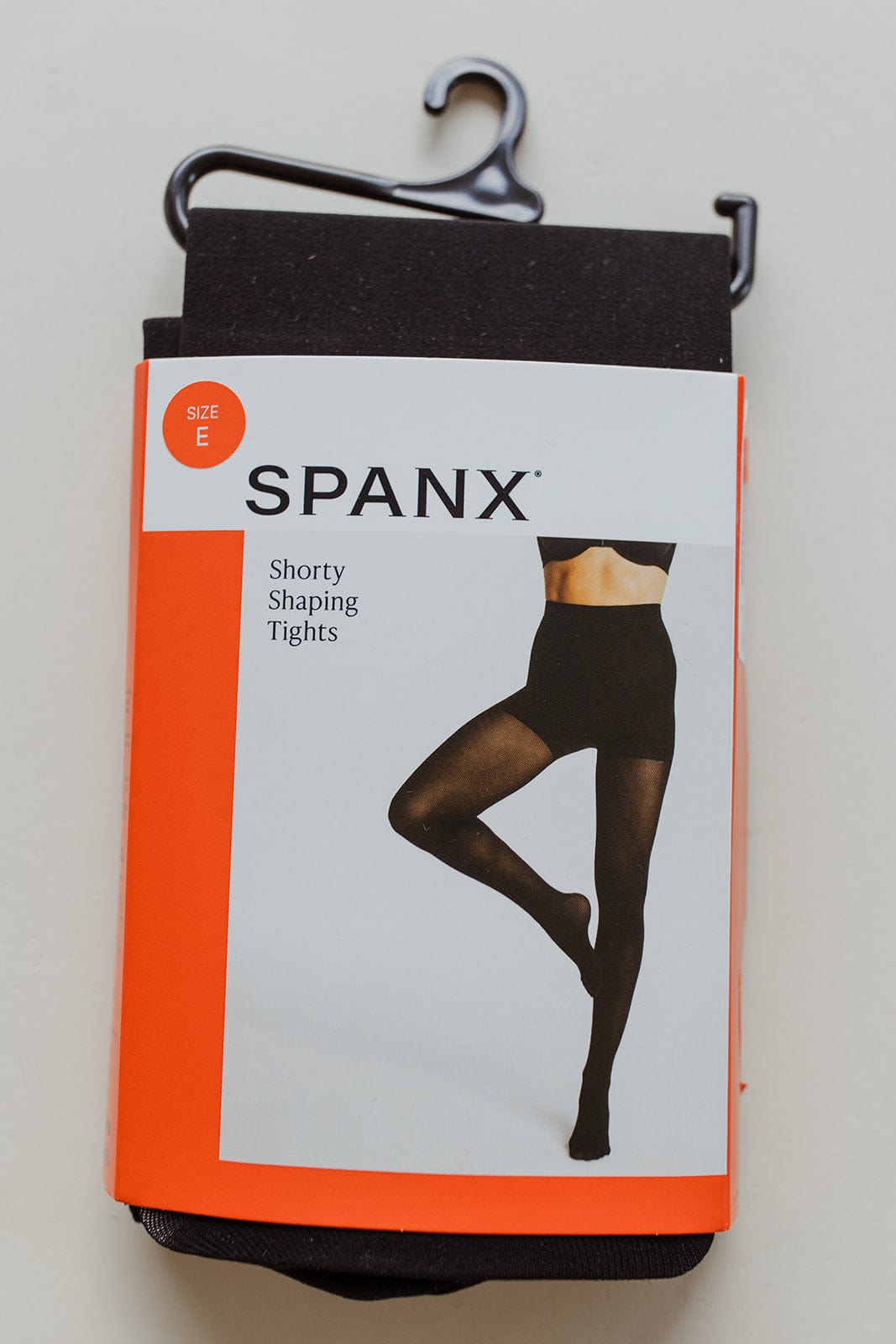 Package of Spanx size E shorty shaping tights with a comfort waistband and black hanger, offering medium support for a secure fit.