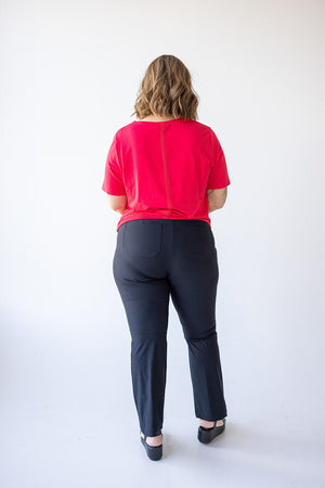 A woman stands with her back to the camera, wearing a red UPF 50+ top and Spanx® Sunshine Kick Flare Pant in Very Black, featuring a 4-way stretch, against a plain white background.