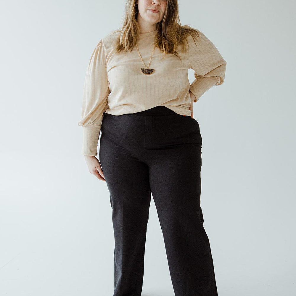 A woman in a beige top and stylish wide-leg pants made from ponte fabric stands against a plain white background, confidently looking at the camera.