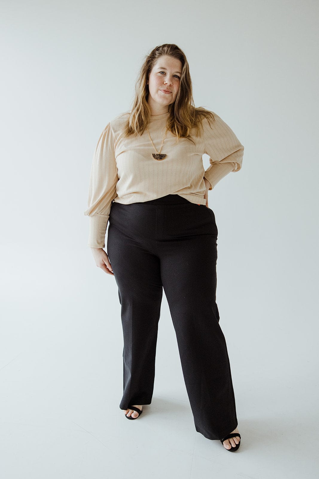 A woman in a beige top and stylish wide-leg pants made from ponte fabric stands against a plain white background, confidently looking at the camera.