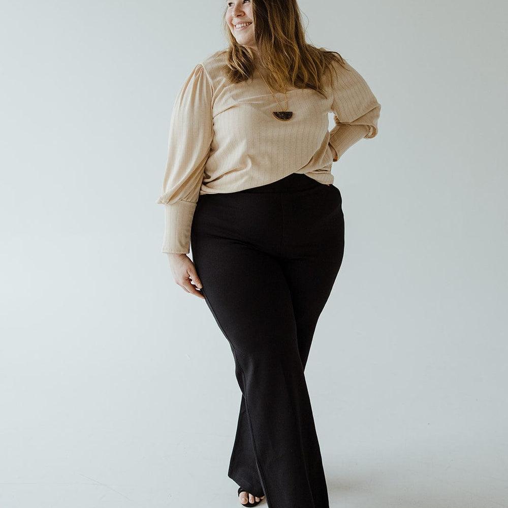 A person wearing a beige top and black wide leg pants in ponte fabric stands confidently, looking to the side, against a plain background.