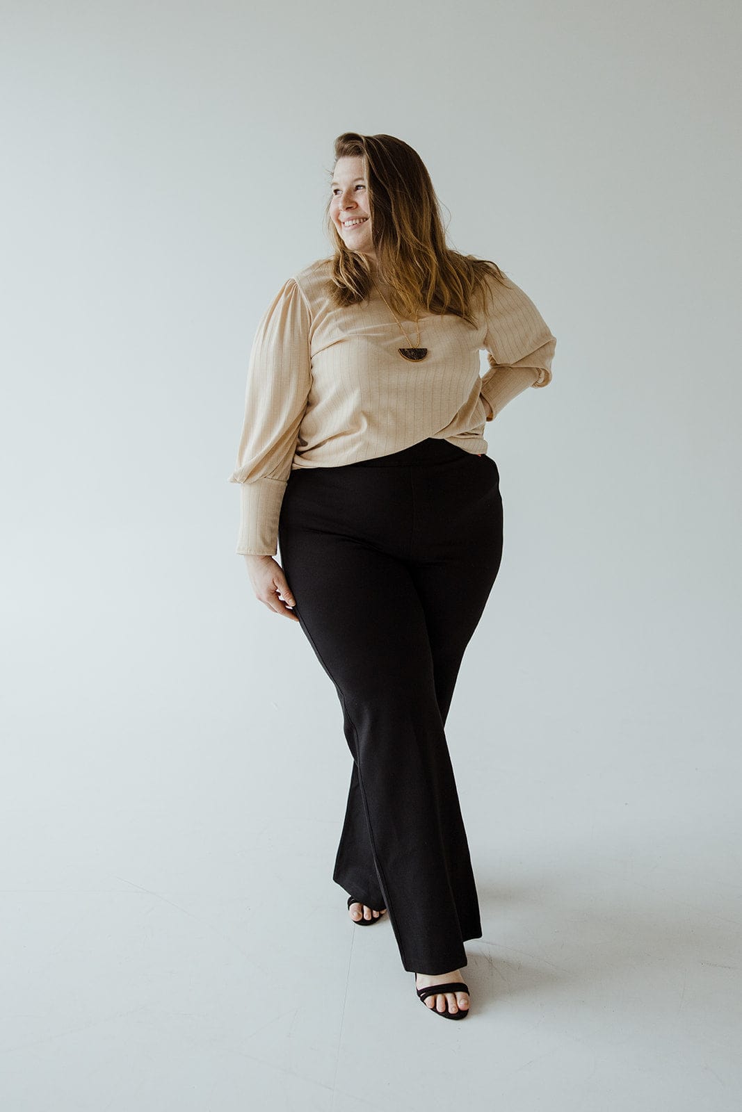 A person wearing a beige top and black wide leg pants in ponte fabric stands confidently, looking to the side, against a plain background.