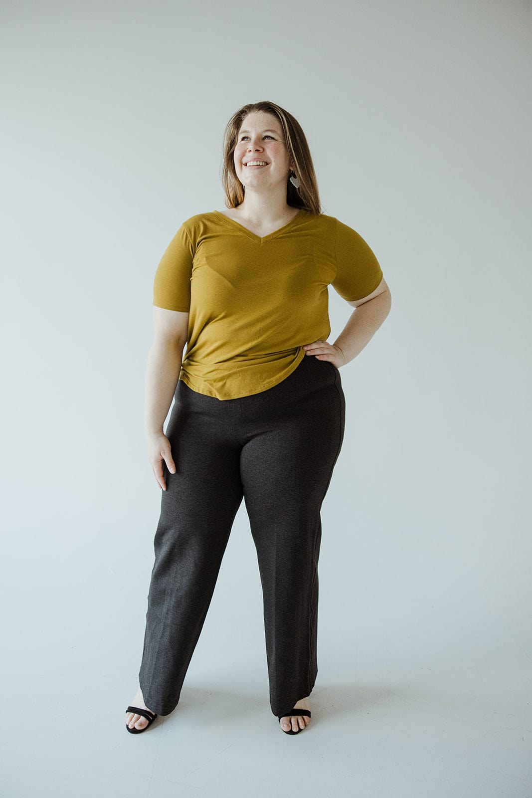 A person radiates confidence in a mustard yellow top and black wide-leg pants crafted from premium ponte fabric. The sleek pull-on design complements their style, as they stand smiling against a plain background.