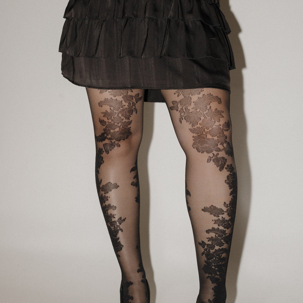 Person wearing a black ruffled dress and floral tights on a plain background SPANX floral tights