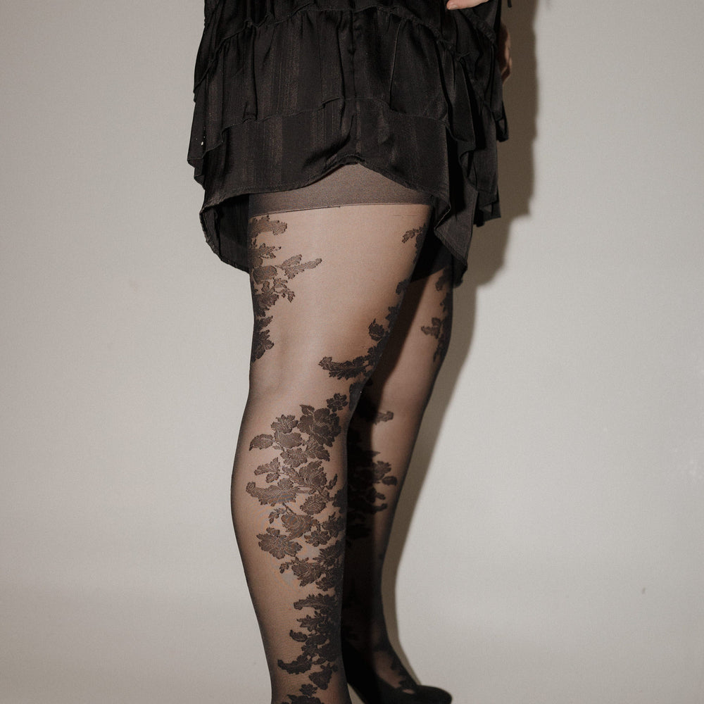 Person wearing a black dress with floral lace stockings and high heels on a plain background SPANX floral tights