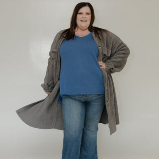 Person wearing a blue shirt, jeans, and a long gray coat against a white background