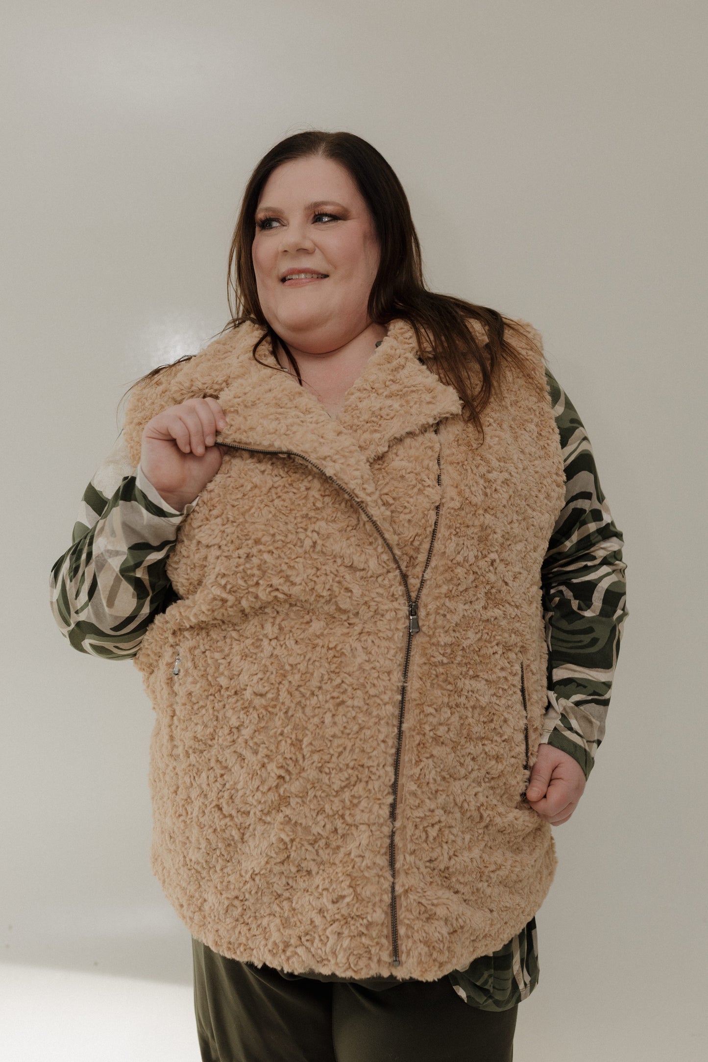 Person wearing a beige fleece vest over a camouflage shirt against a plain background