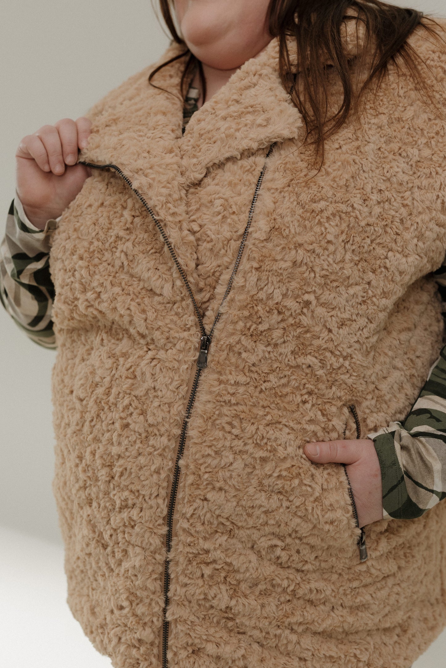 Person wearing a beige sherpa vest with a neutral background