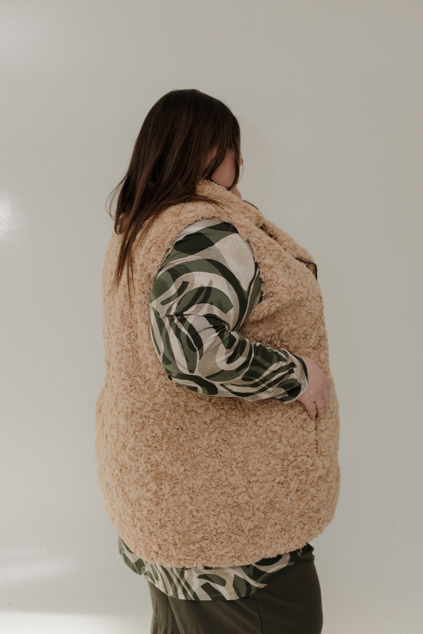 Person wearing a beige fleece vest over a patterned shirt on a plain background