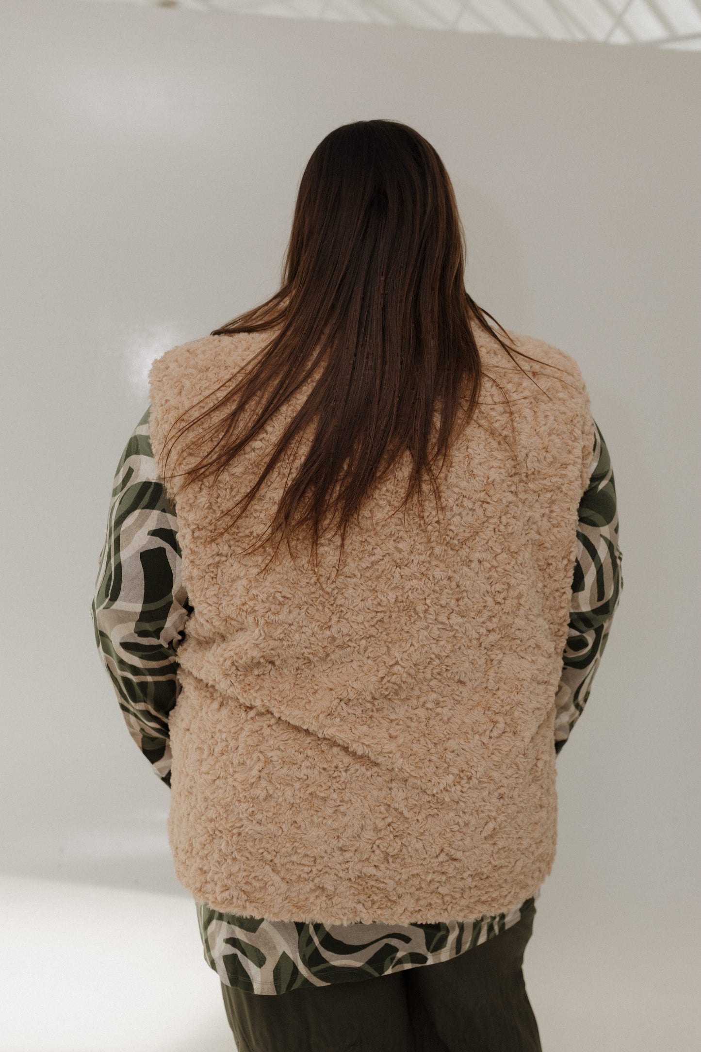 Person wearing a beige fleece vest over a patterned shirt on a plain background