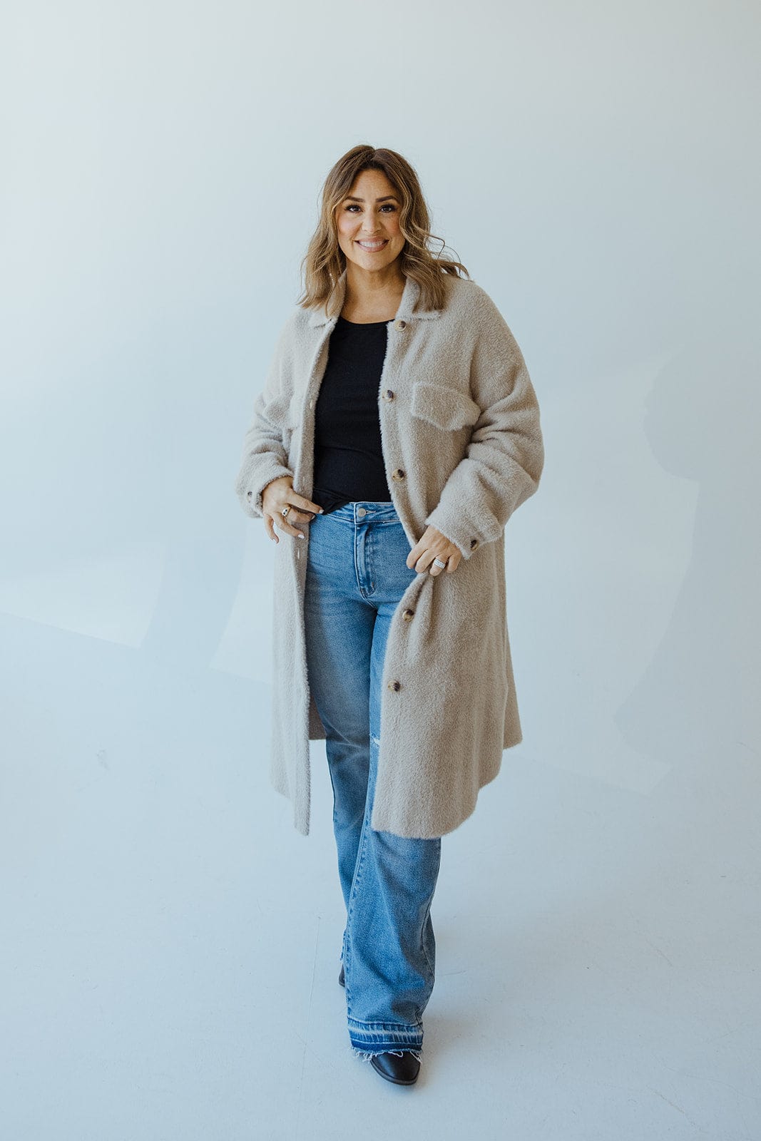 A person wearing a cozy shacket over a black top and blue jeans stands on a white background, exuding effortless style.