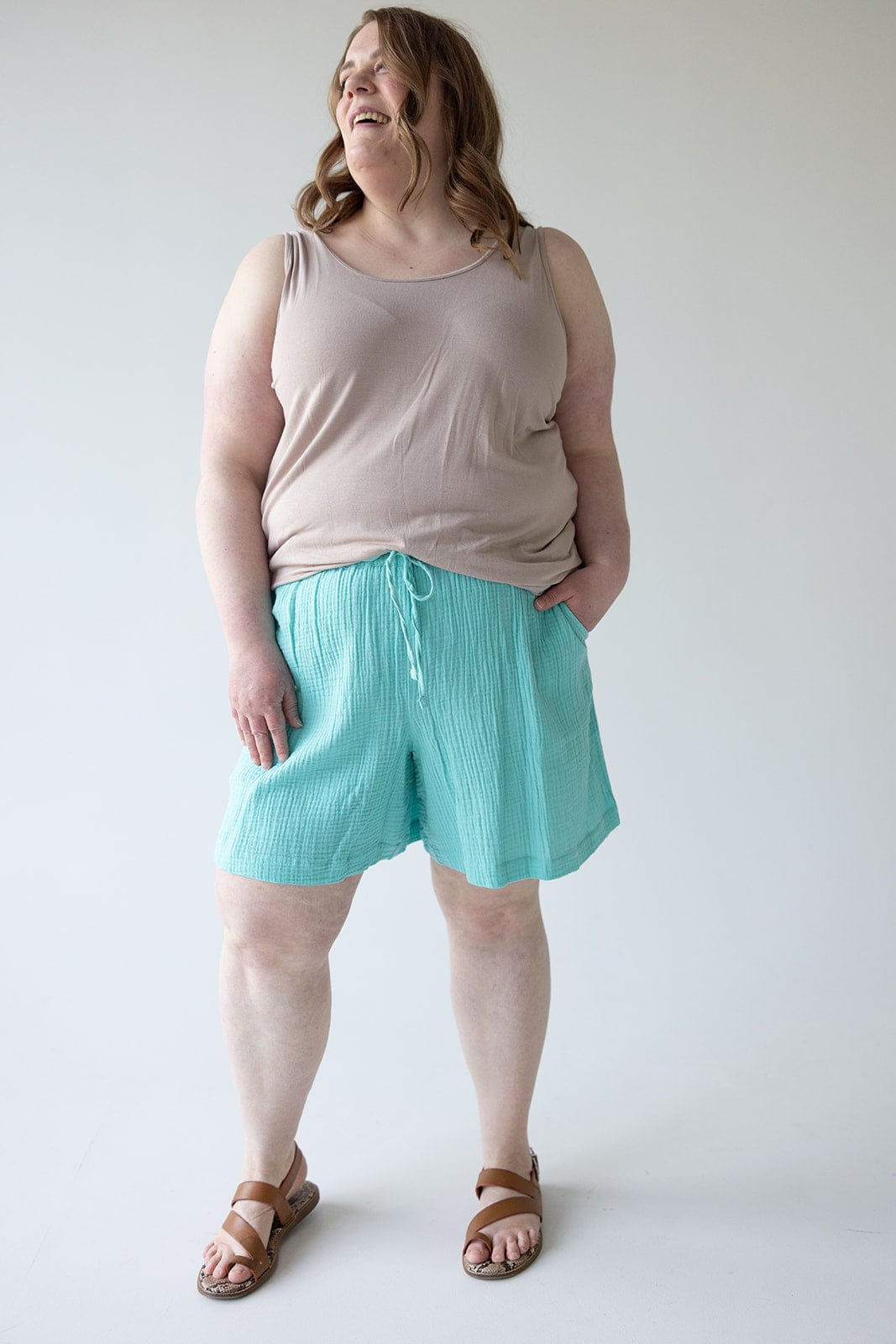 A person stands against a plain background wearing a beige tank top, Maui Textured Cotton Shorts with an elastic waistband, and brown sandals.