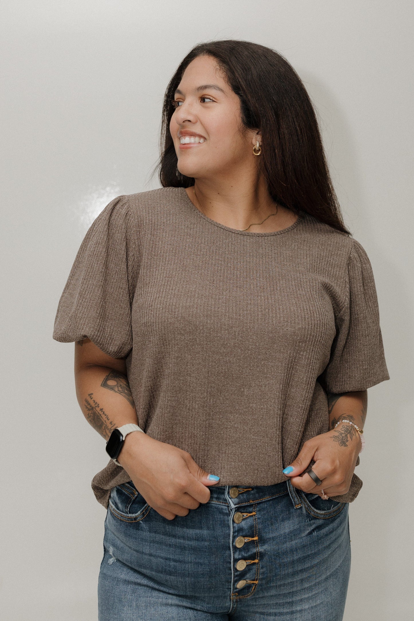 Woman wearing a brown top and blue jeans against a plain background