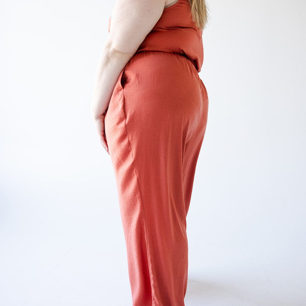 A person wearing Textured Wide Leg Satin Pants in Copper from Love Marlow, paired with black sandals, stands sideways in a minimalist setting.