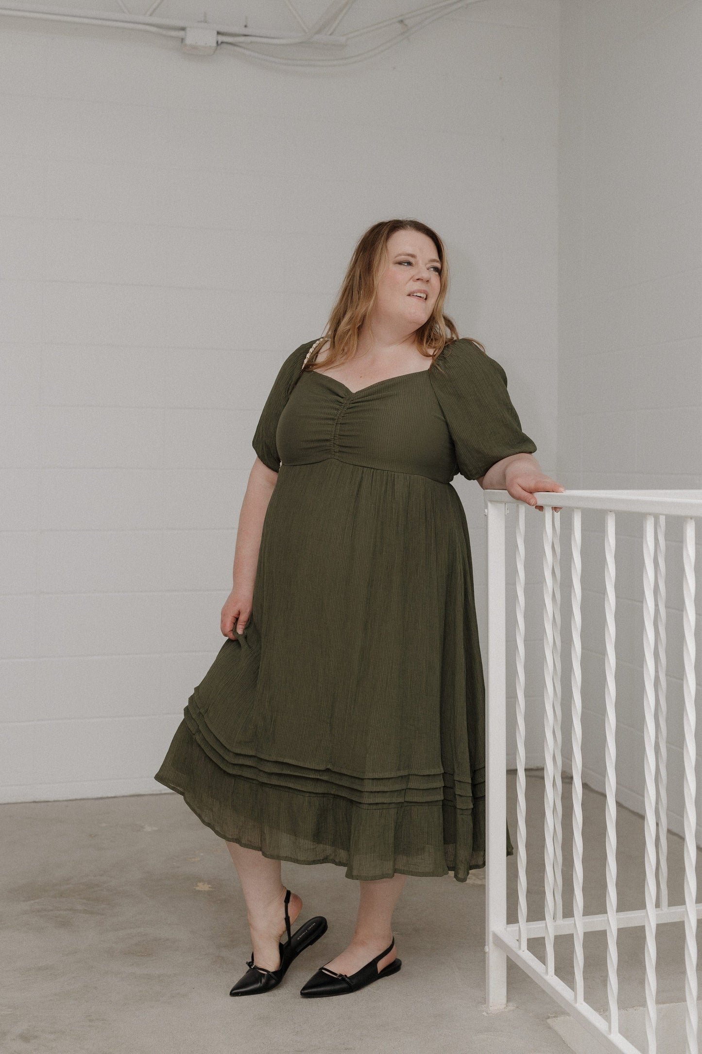 Woman wearing a green dress standing next to a white railing indoors.