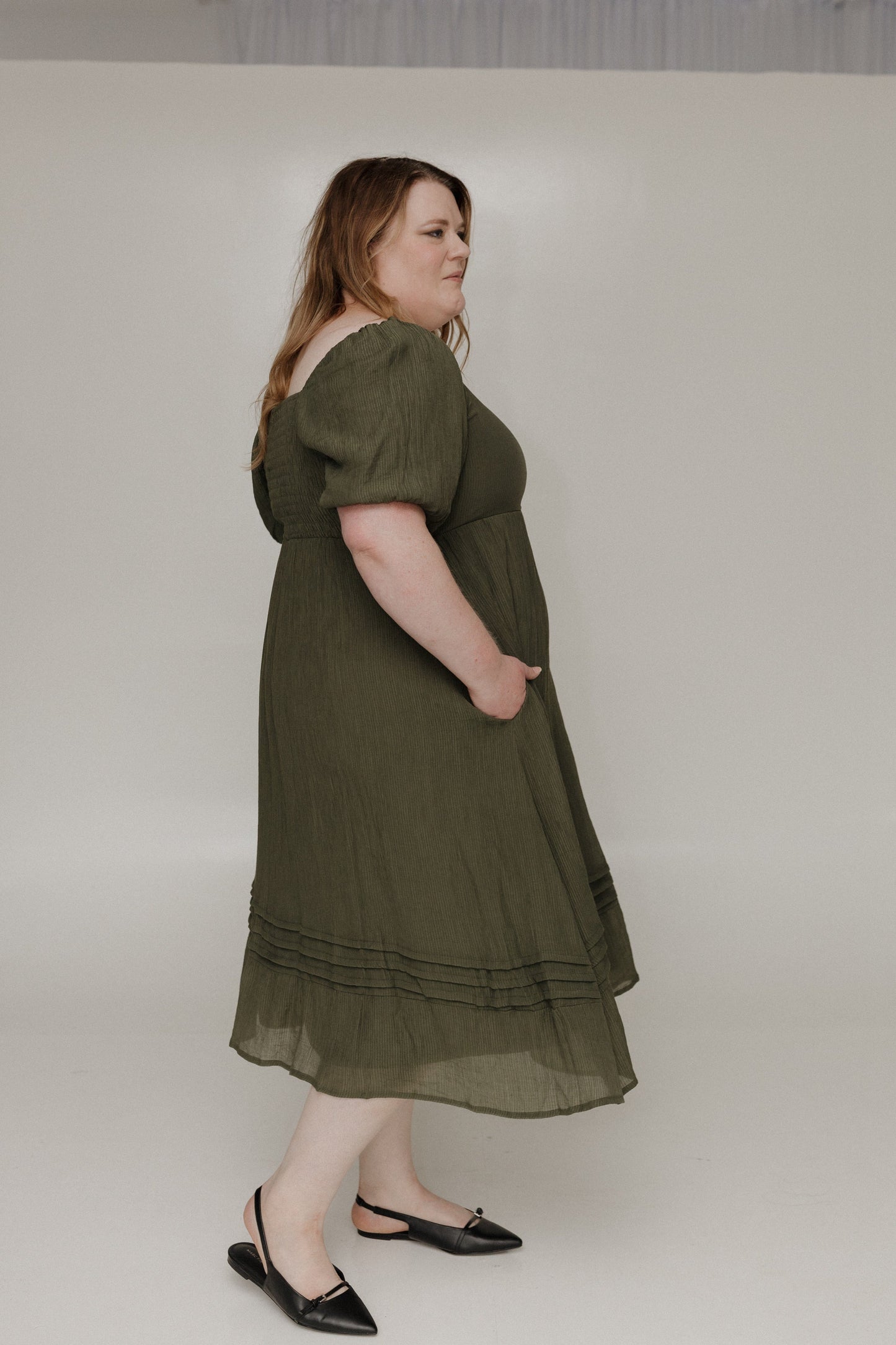 Woman wearing an olive green dress against a plain background