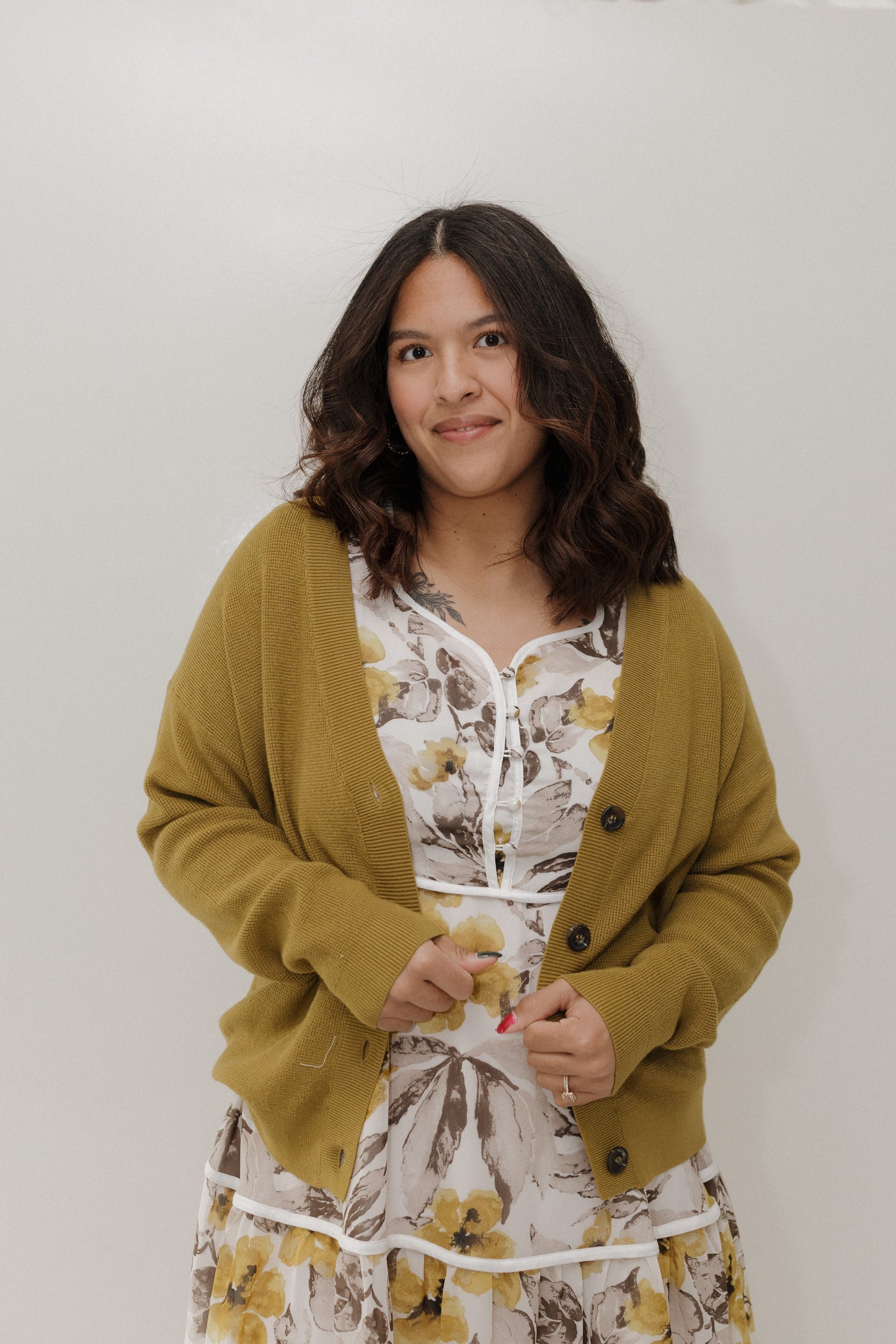 Woman wearing a mustard yellow cardigan over a floral dress against a white background