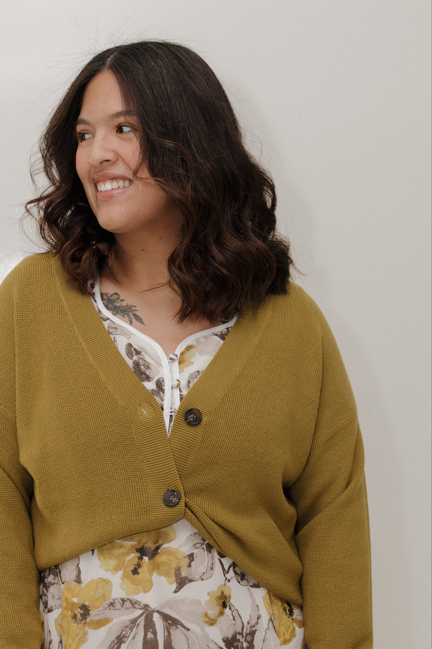 Woman wearing a mustard yellow cardigan over a floral dress against a plain background