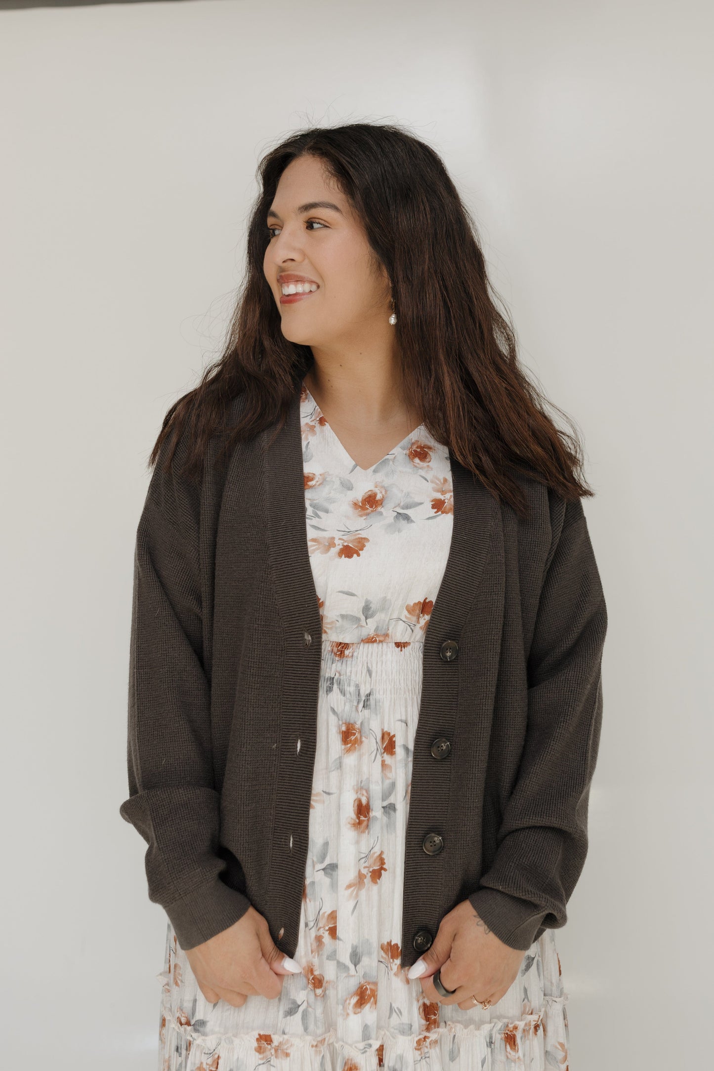 Woman wearing a dark brown cardigan over a floral dress against a white background