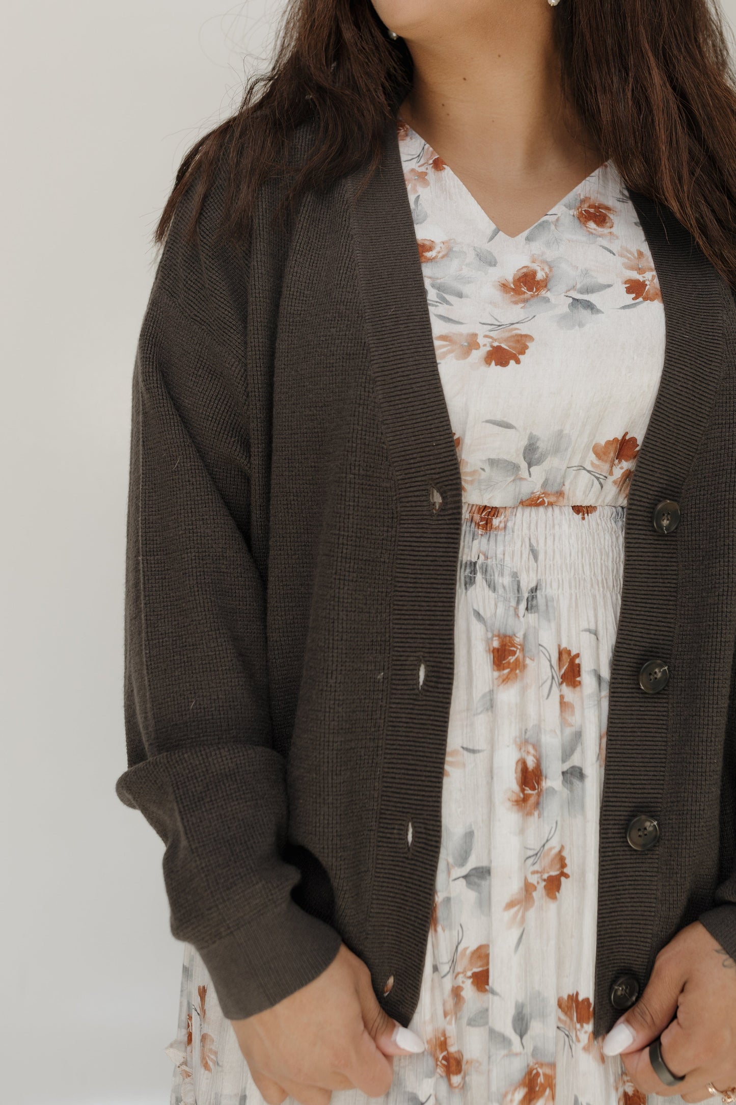 Person wearing a brown cardigan over a floral dress against a plain background