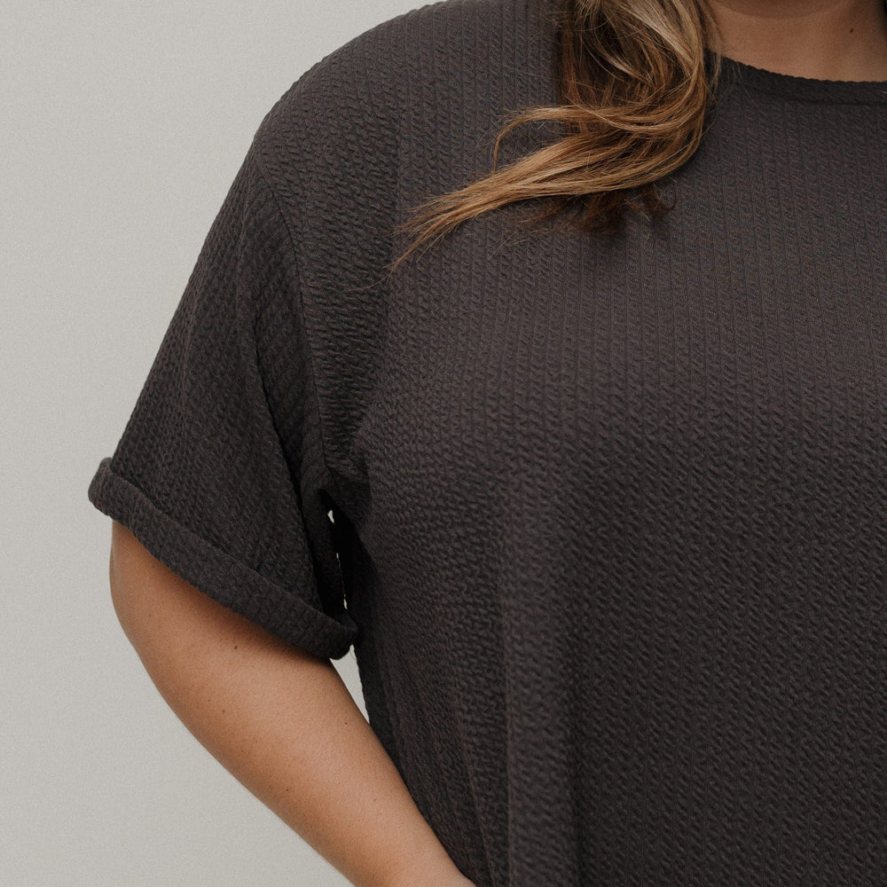 Person wearing a dark brown t-shirt against a plain background