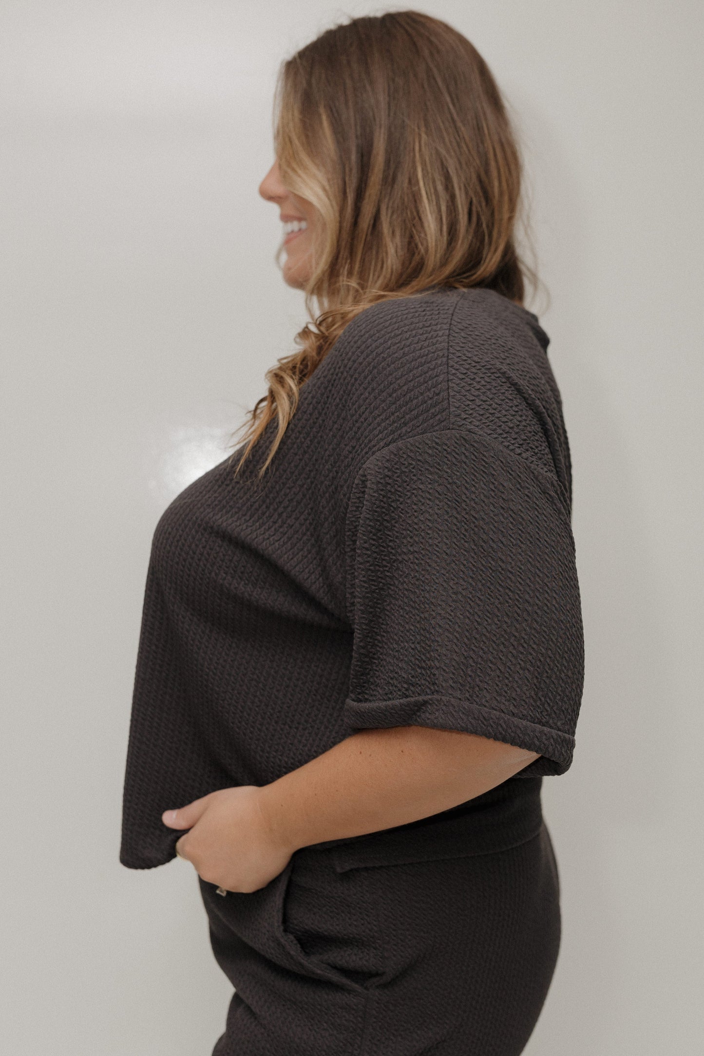 Woman wearing a dark gray textured top against a plain background