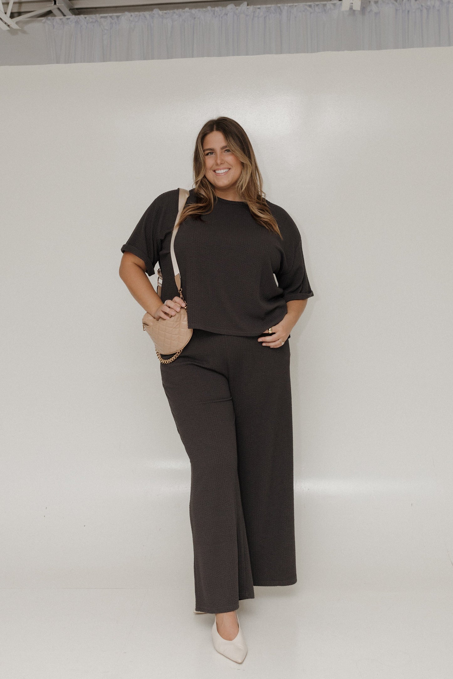 Woman wearing a black outfit with a beige bag against a white background