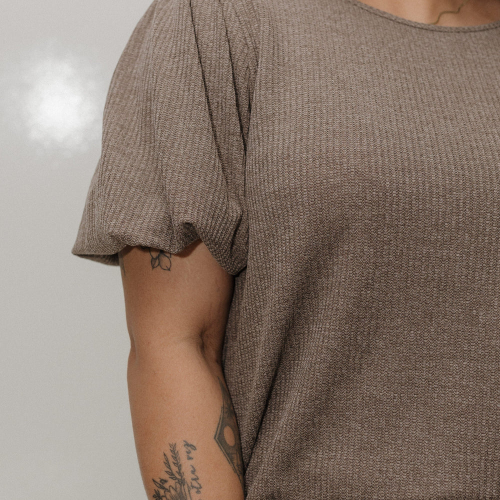 Person wearing a brown textured top and blue jeans with a neutral background