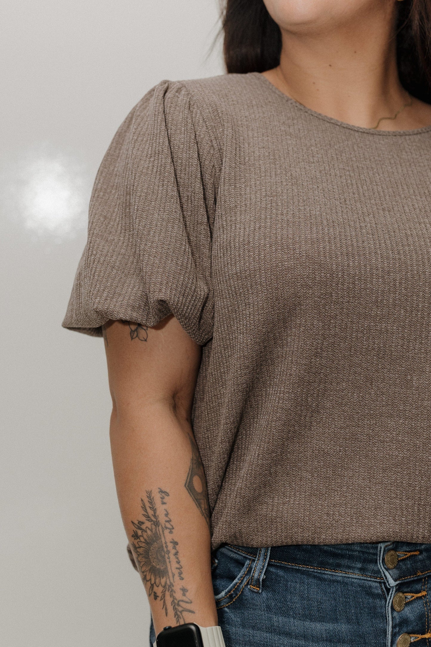 Person wearing a brown textured top and blue jeans with a neutral background
