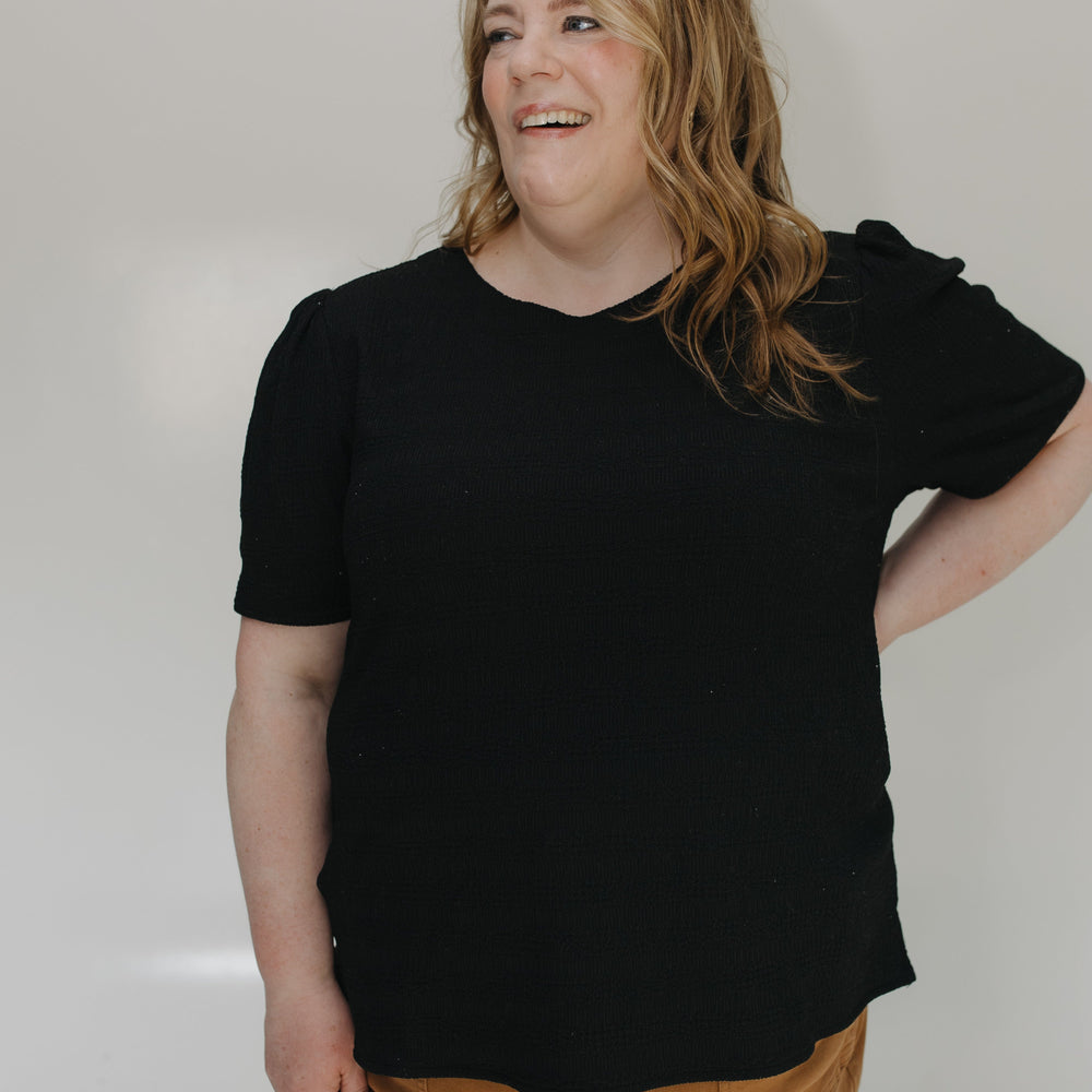 Person wearing a black t-shirt and brown pants against a white background