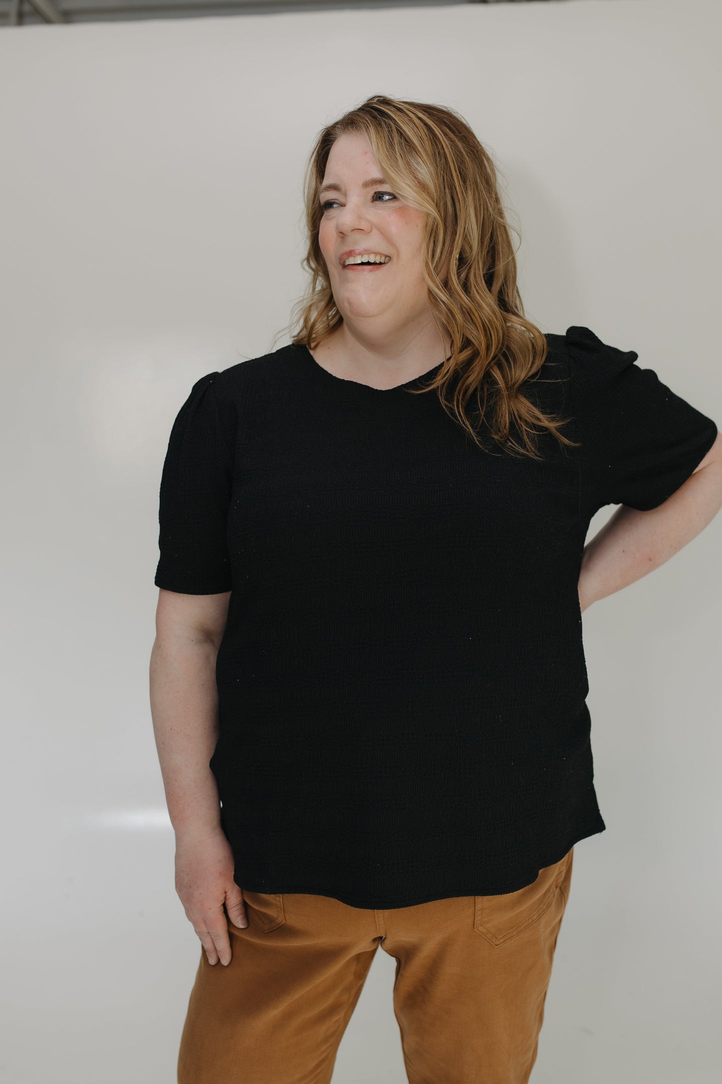 Person wearing a black t-shirt and brown pants against a white background