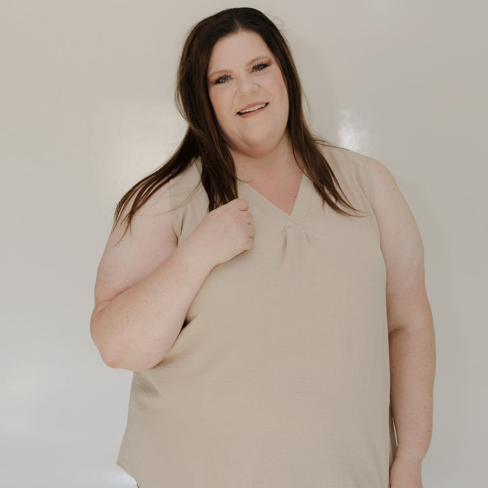 Woman wearing a beige top and blue jeans against a plain background