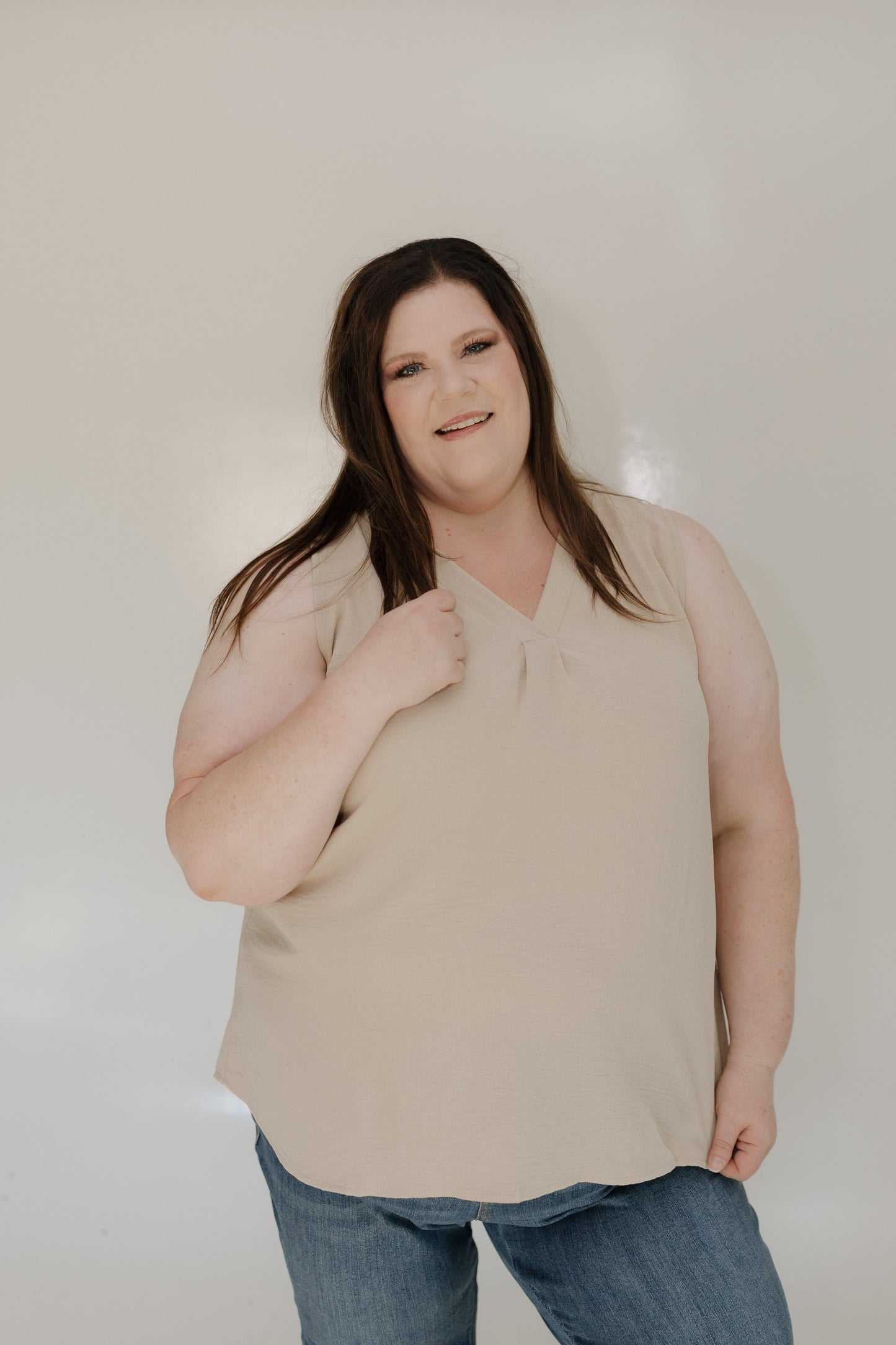 Woman wearing a beige top and blue jeans against a plain background