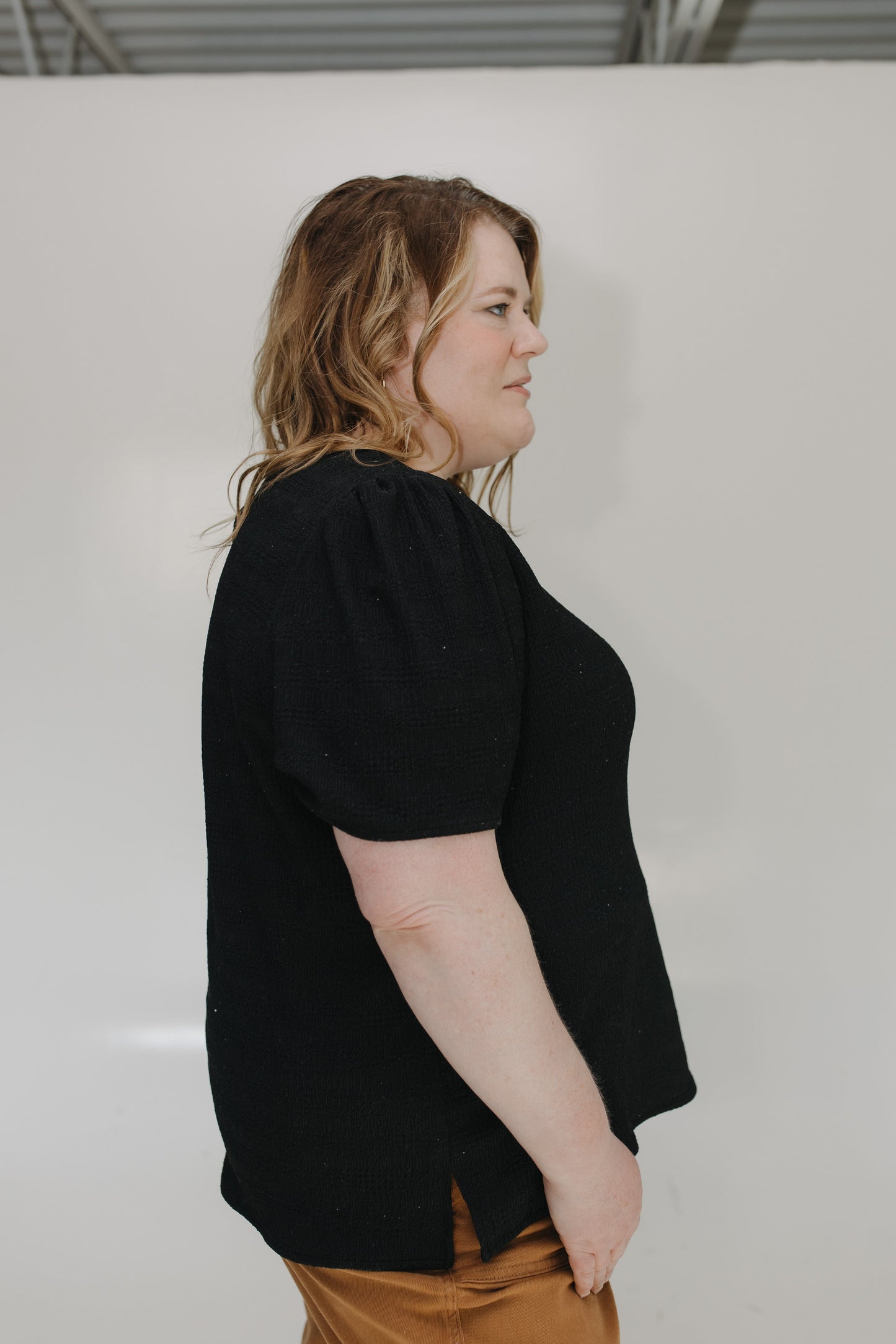 Person wearing a black shirt and brown pants against a white background