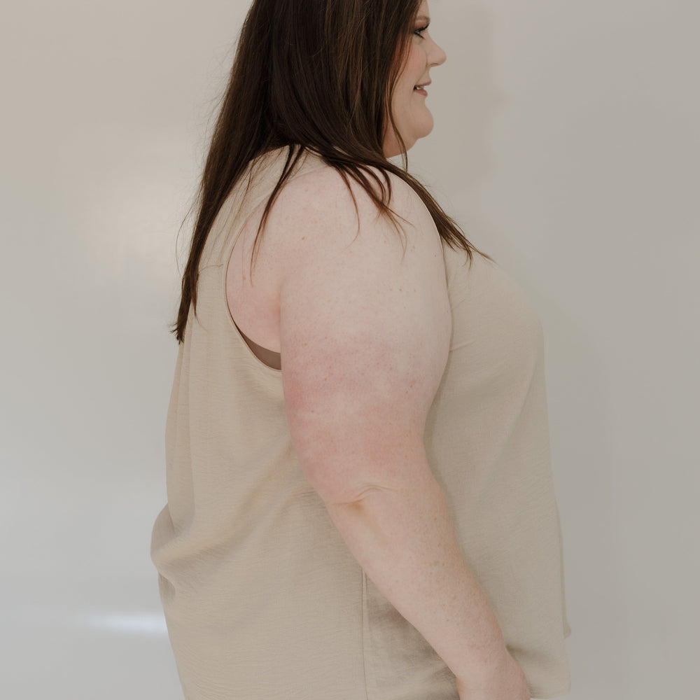 Woman wearing a beige sweater and blue jeans against a plain background