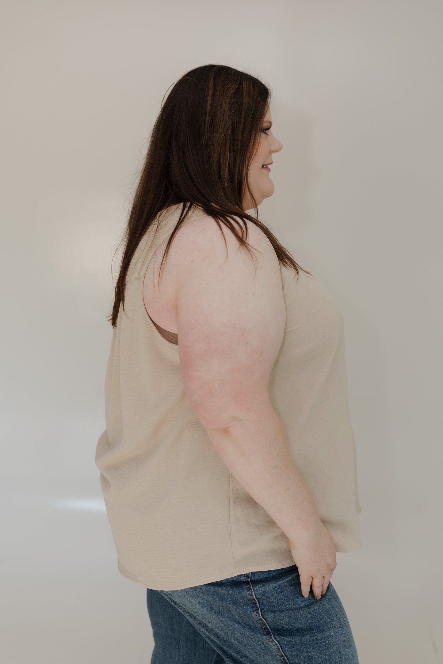 Woman wearing a beige sweater and blue jeans against a plain background