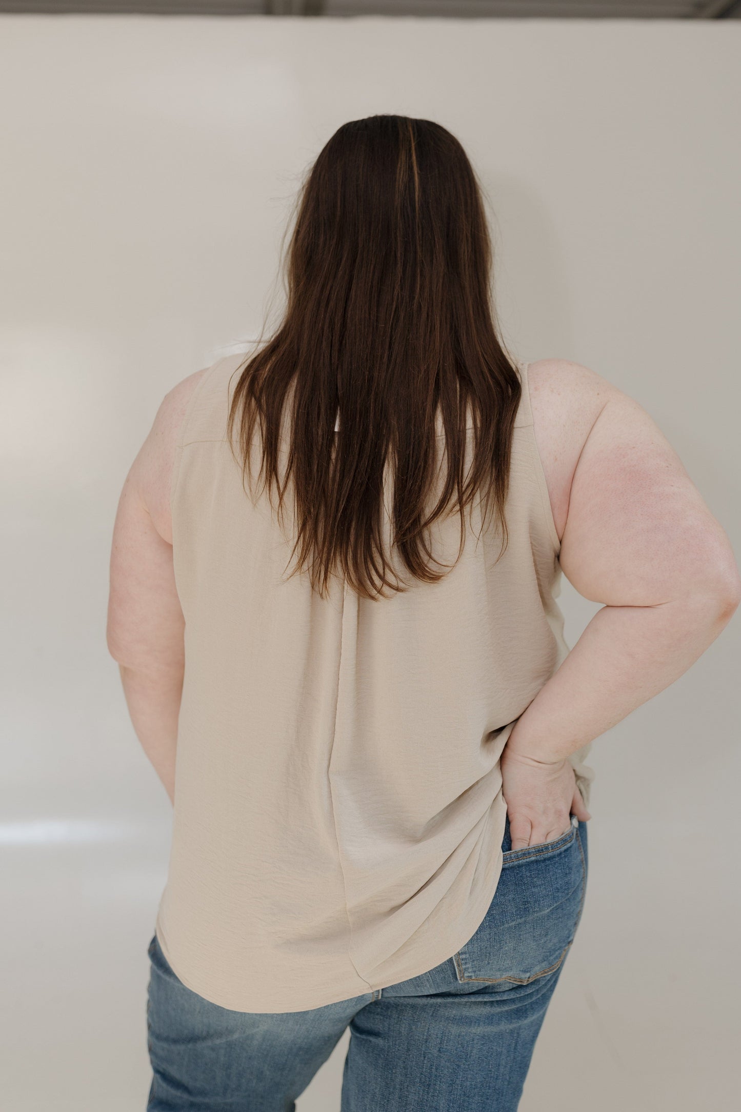 Person wearing a beige sleeveless top and blue jeans against a plain background