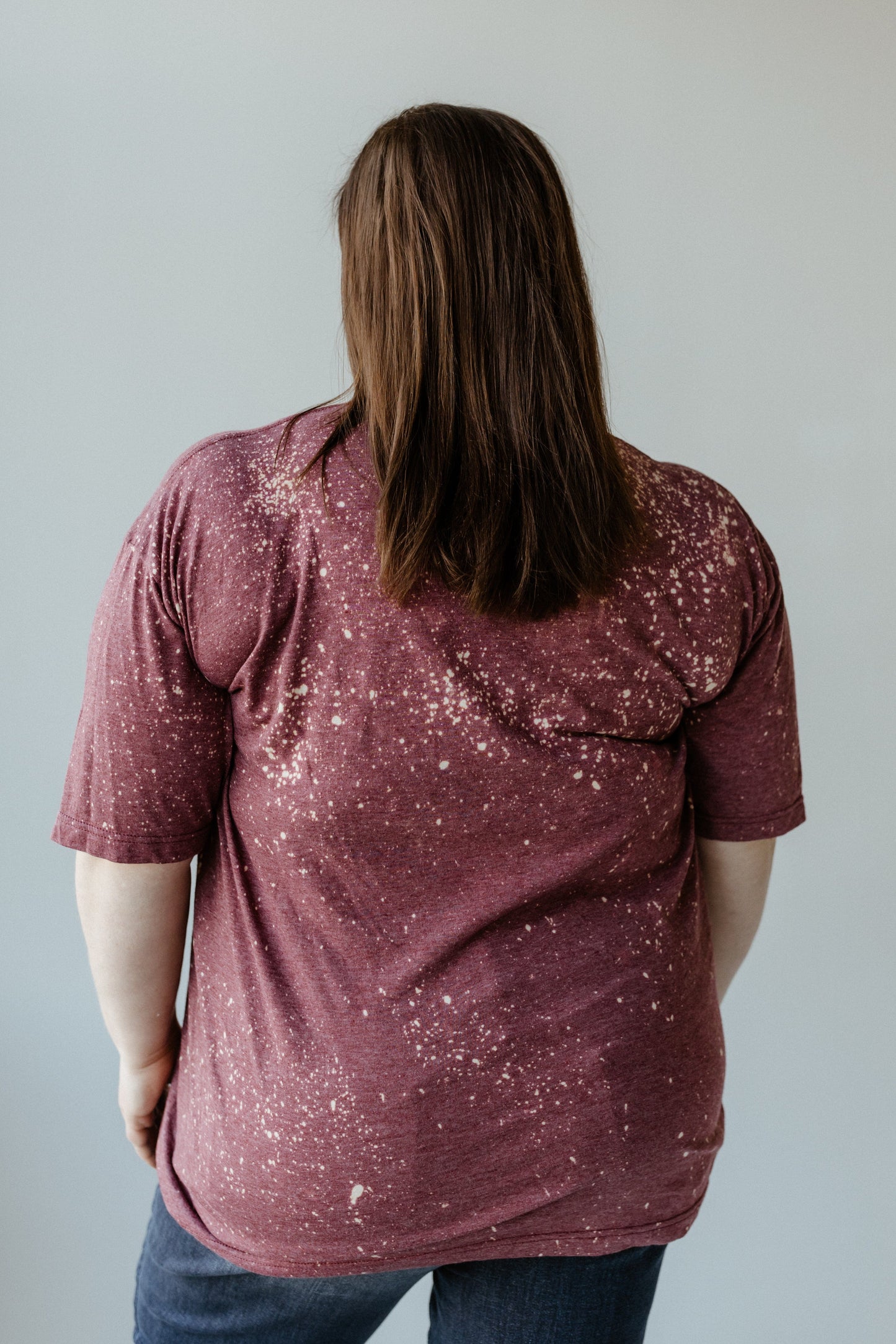 A person with long brown hair, wearing a maroon speckled T-shirt that looked almost hand bleached, is facing away from the camera.
